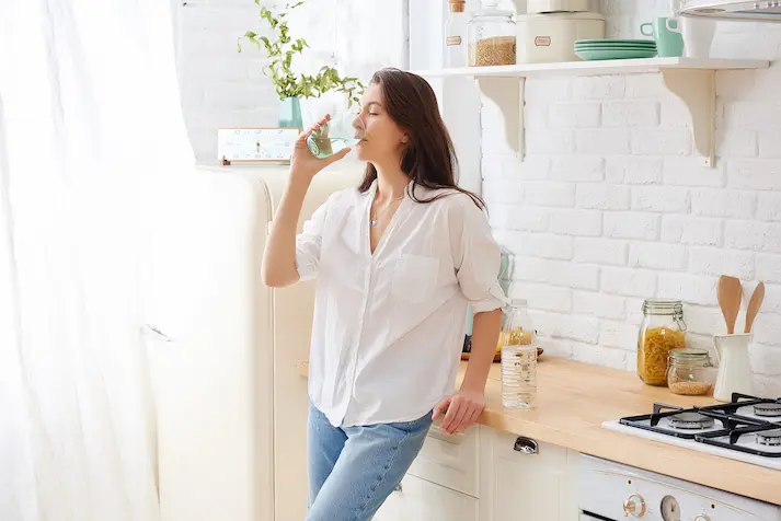 Woman leaning on a kitchen counter drinking a glass of water
